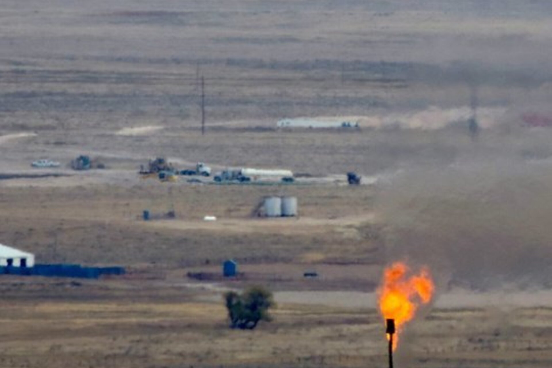 A torch on fire with trucks in the background in a dry landscape