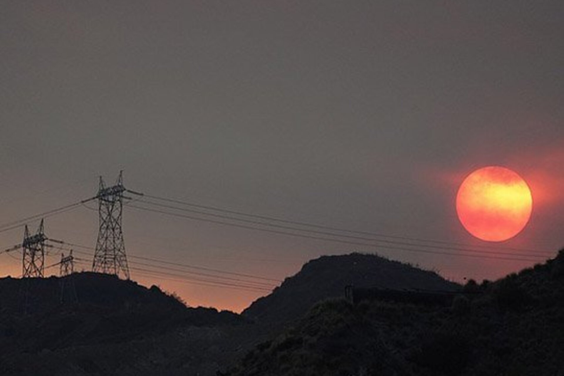 An orange sun peeks through a very hazy, grey sky