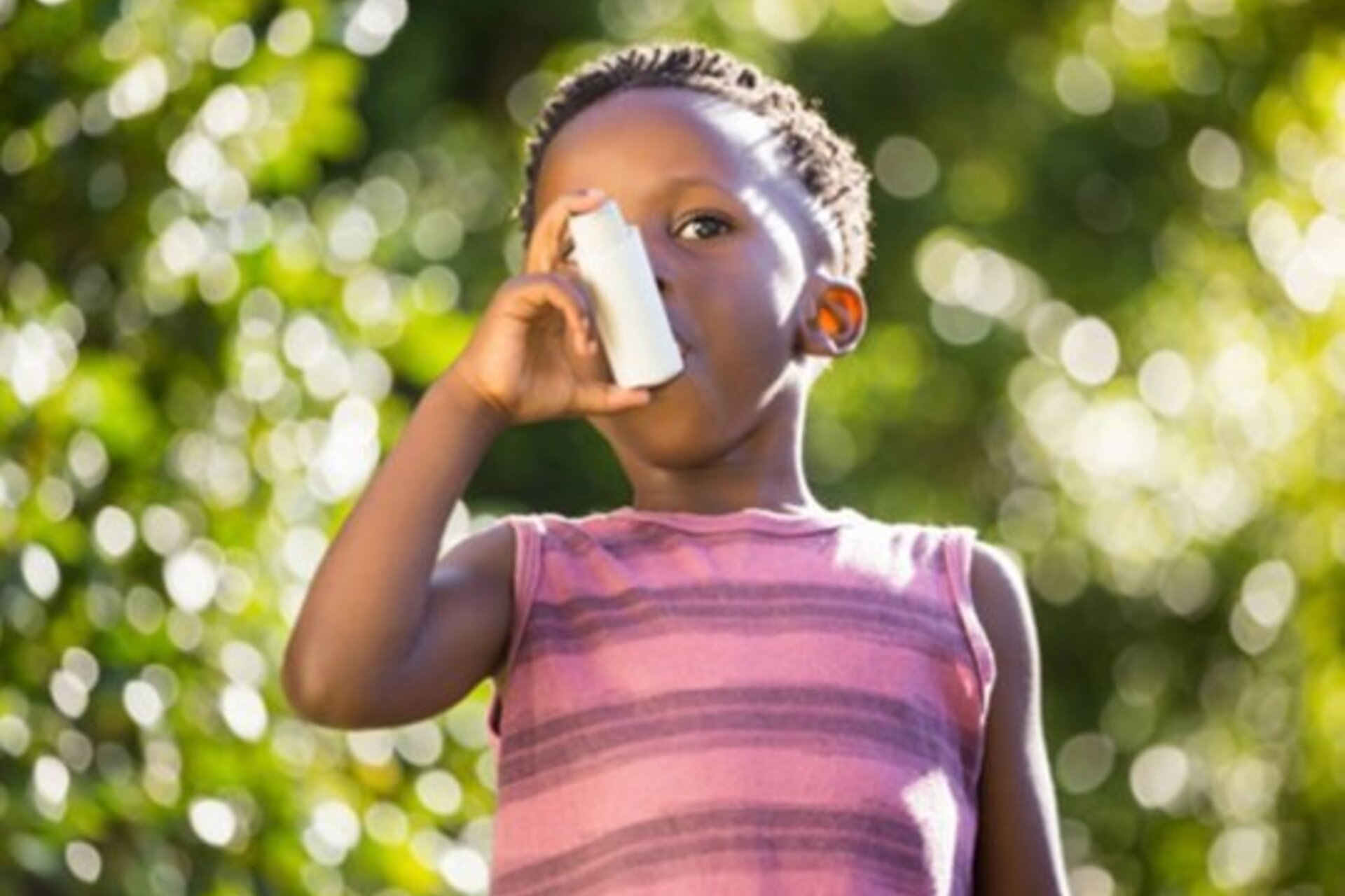 A young child holds his inhaler up to his mouth