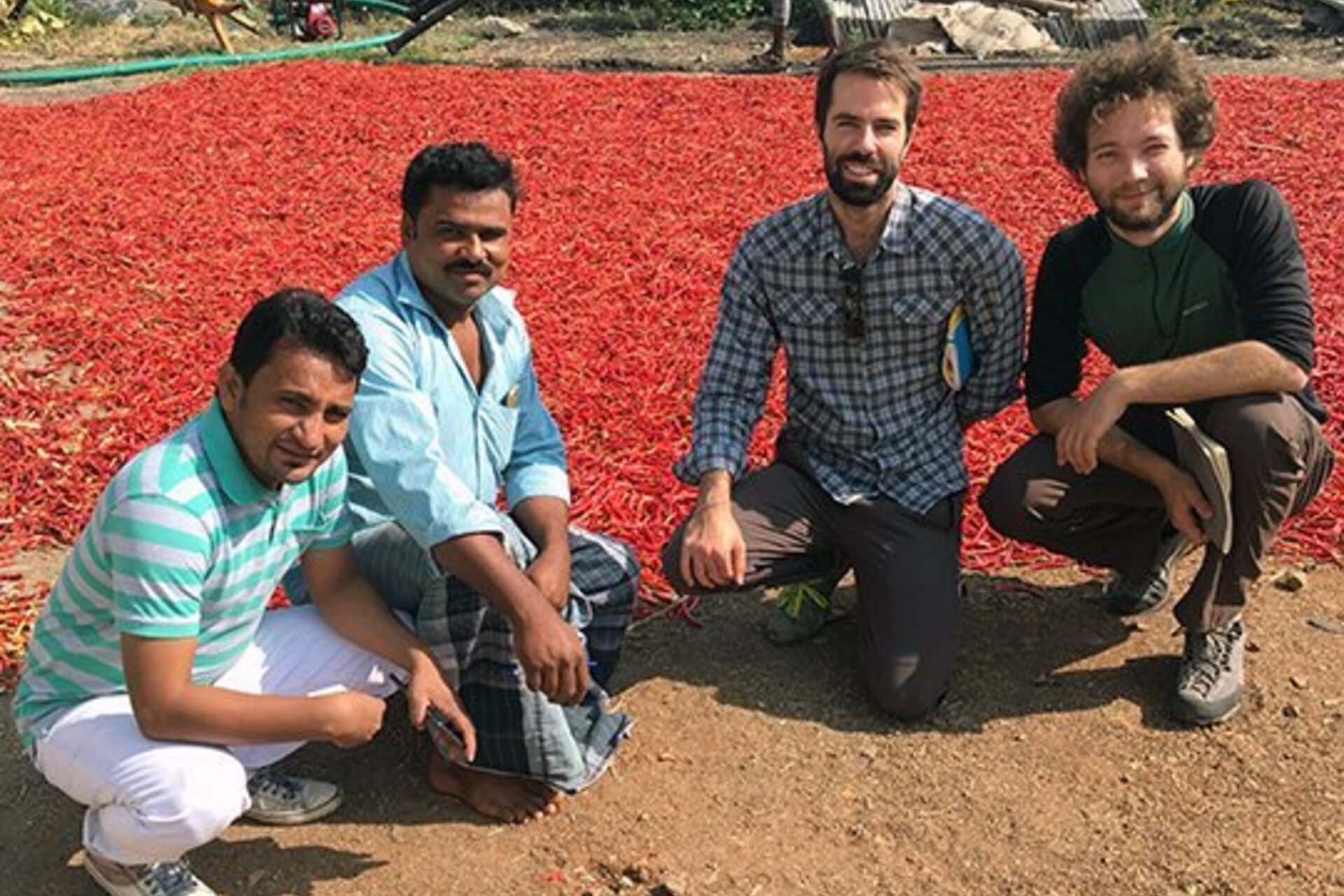 Researchers pose for a photo next to an area with many red chiles air drying