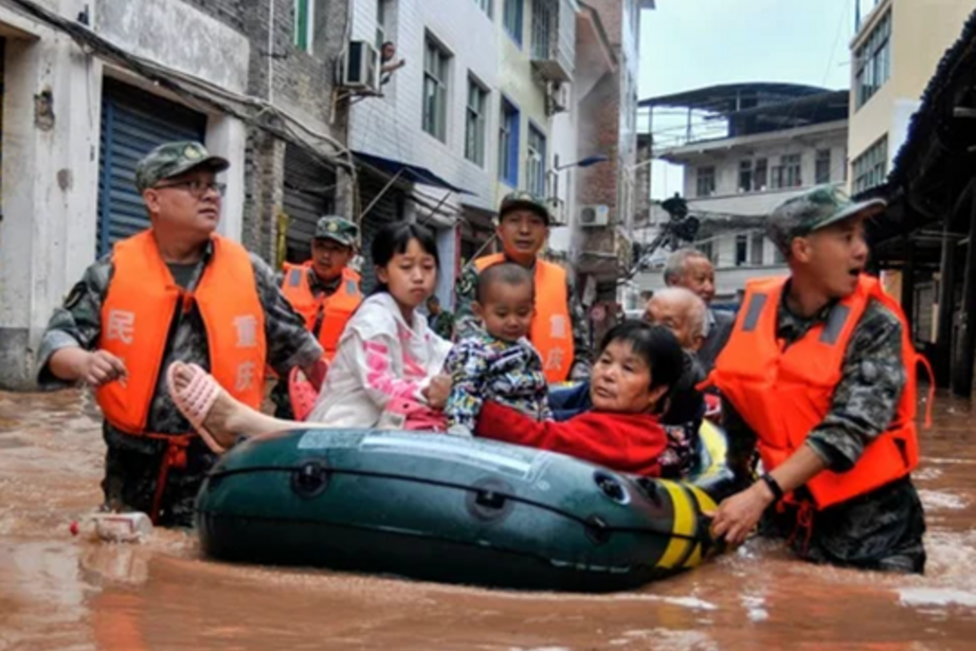 People in a raft in a flooded street in China, being helped in officials wearing bright vests