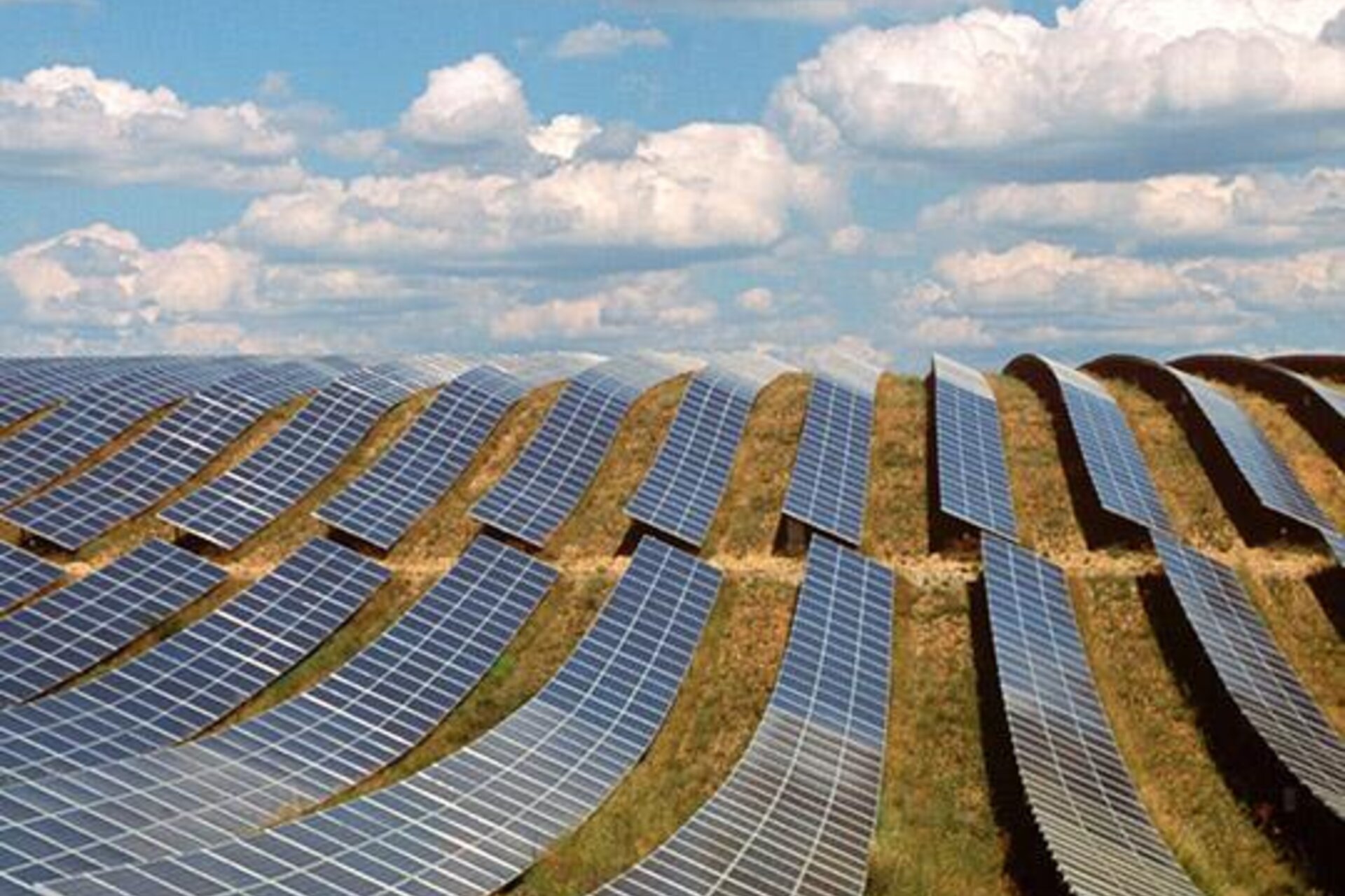 Rows of many solar panels along a sloped field on a sunny day with fluffy clouds in the sky