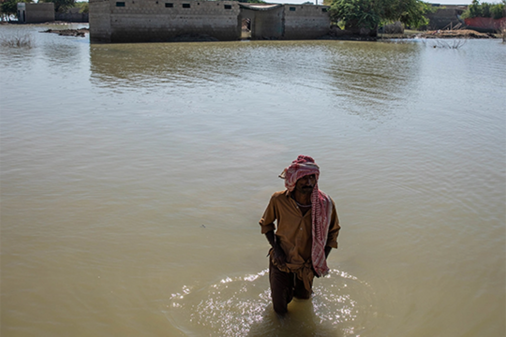 A man wades through floodwater in Pakistan that left millions of people dispossessed of land and lacking food, water, or work this past October 2022
