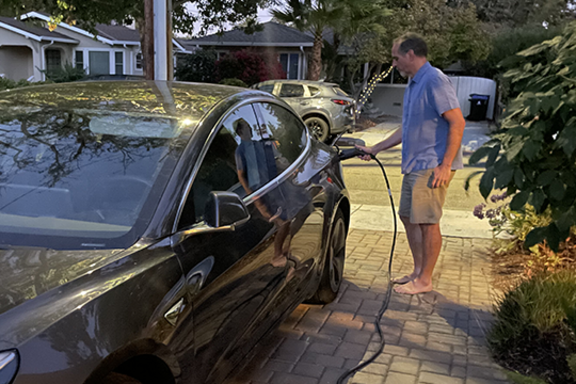 A man charges his Tesla in the driveway of his home