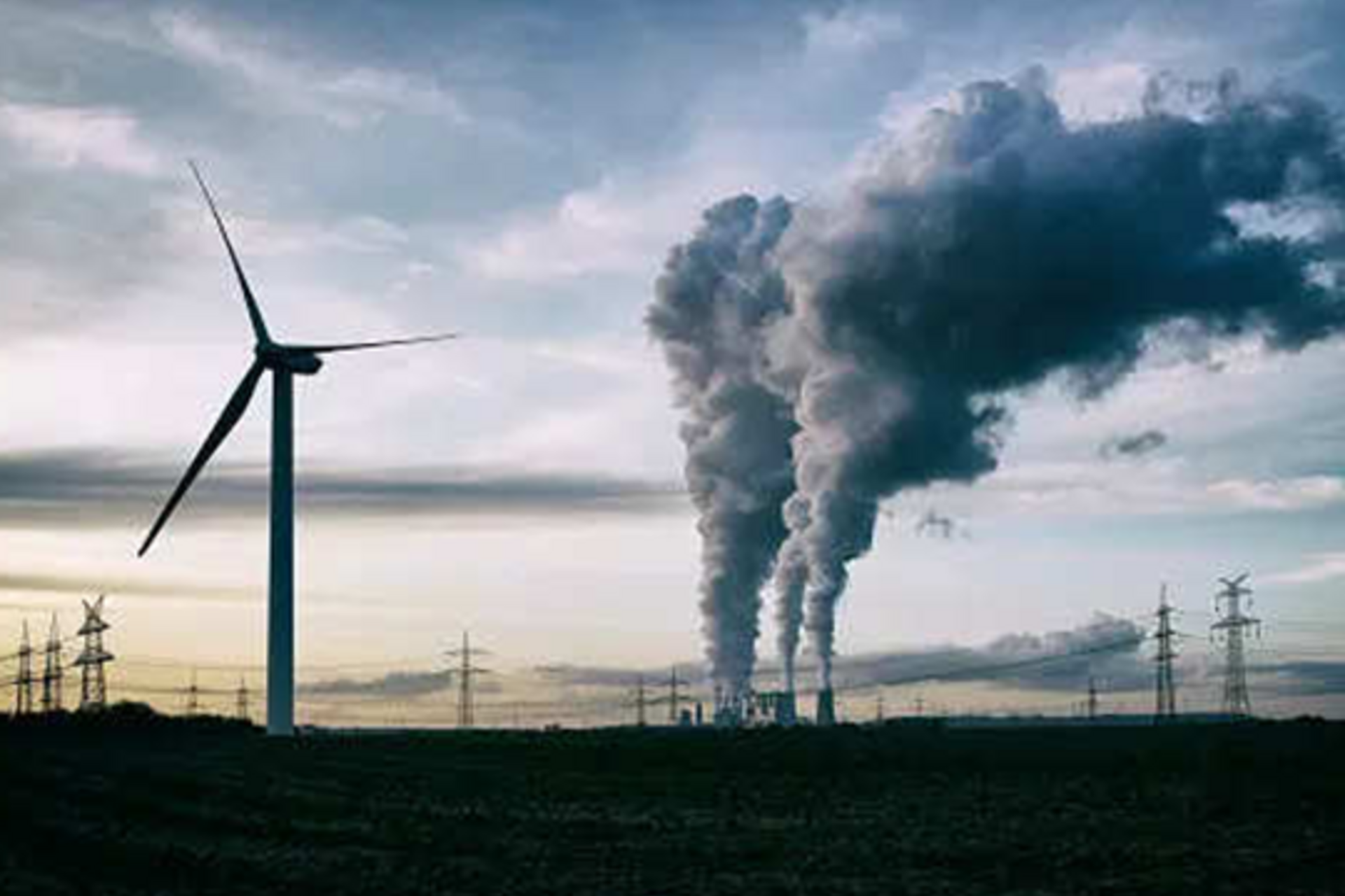 A coal plant releasing emissions next to wind turbines