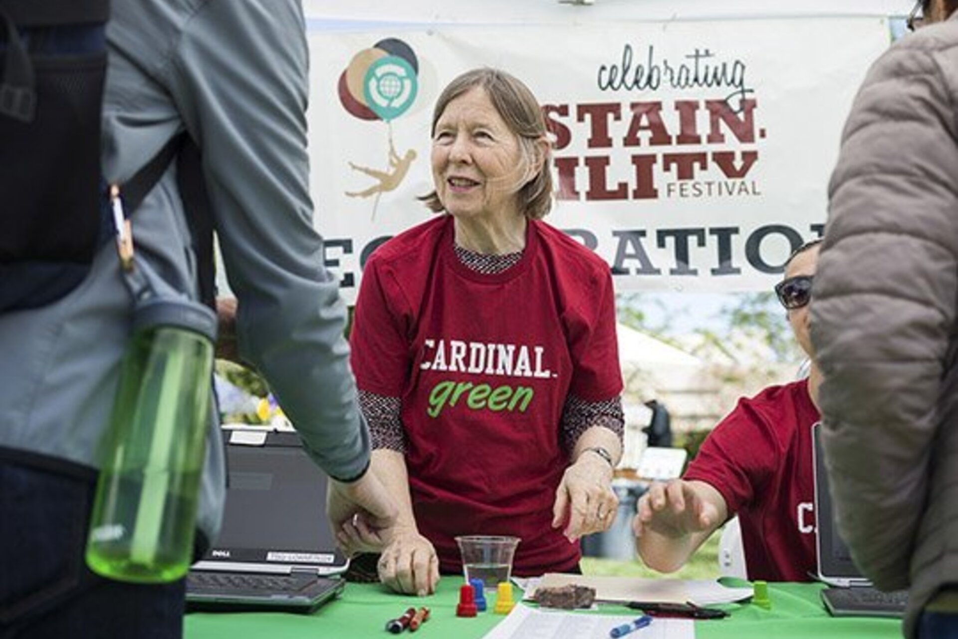 A woman wearing a Cardinal Green T-shirt at a table where they are greeting event attendees