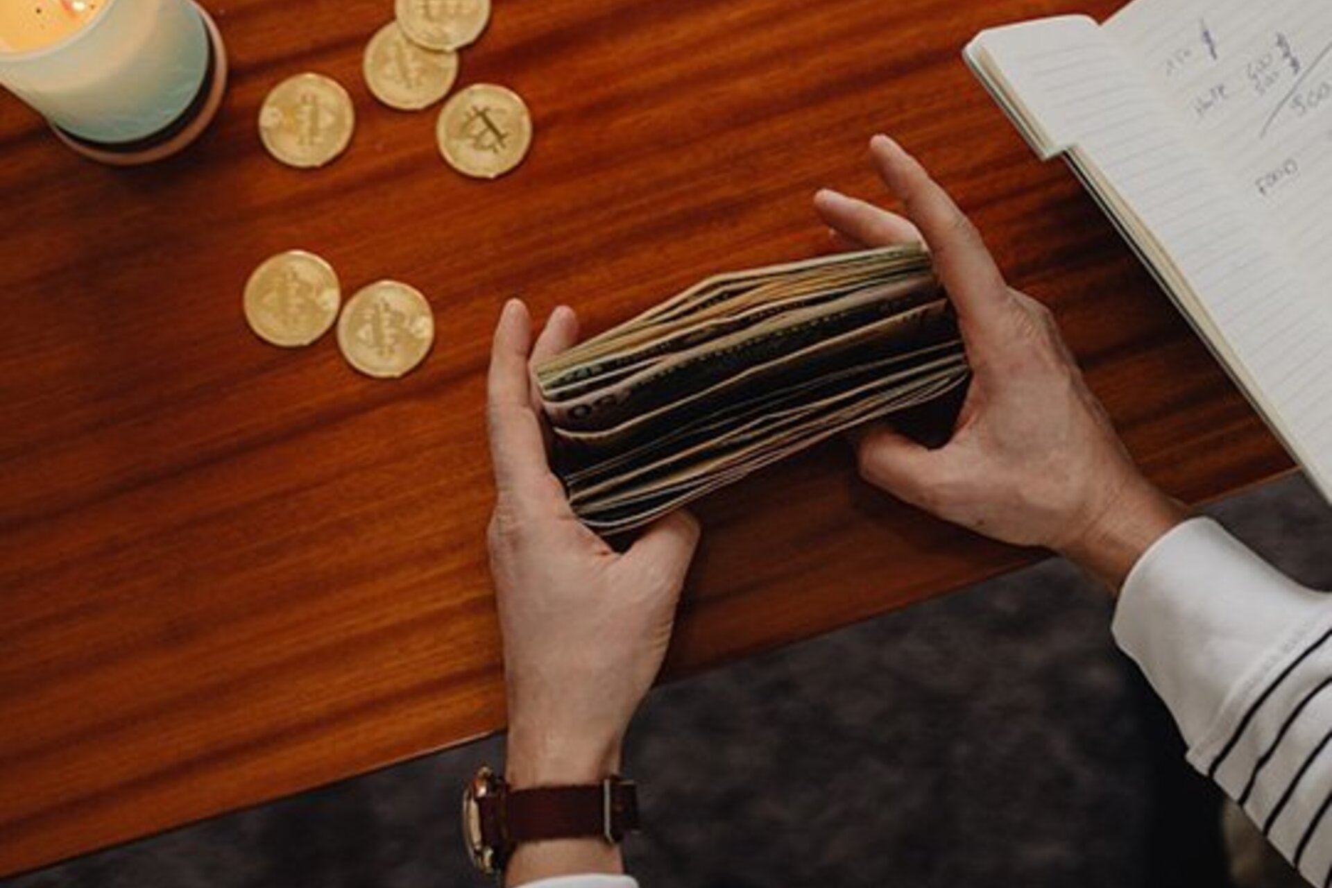 A person holding dollar bills with coins on the table