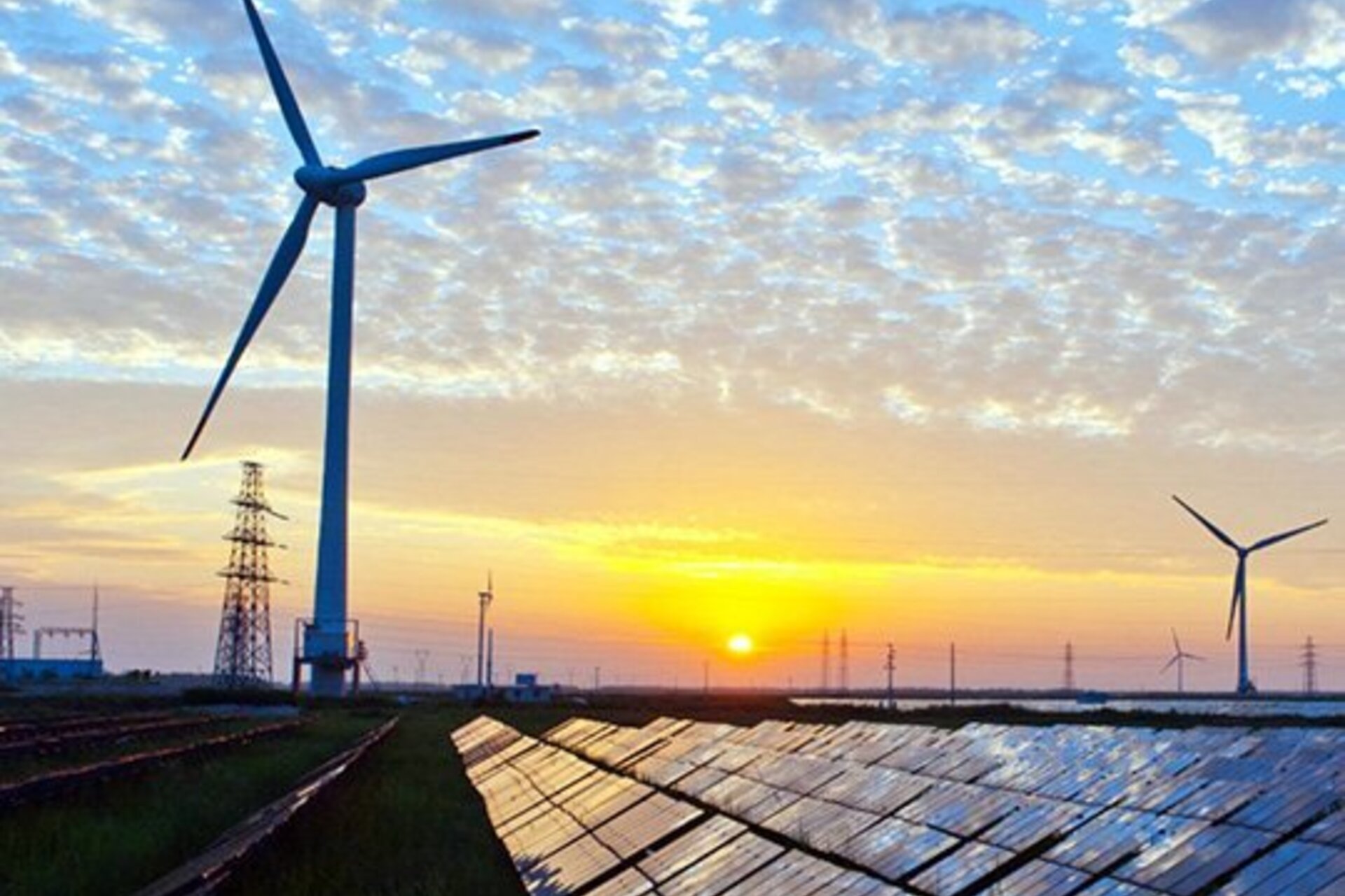 Wind turbines next to a solar panel field during sunset