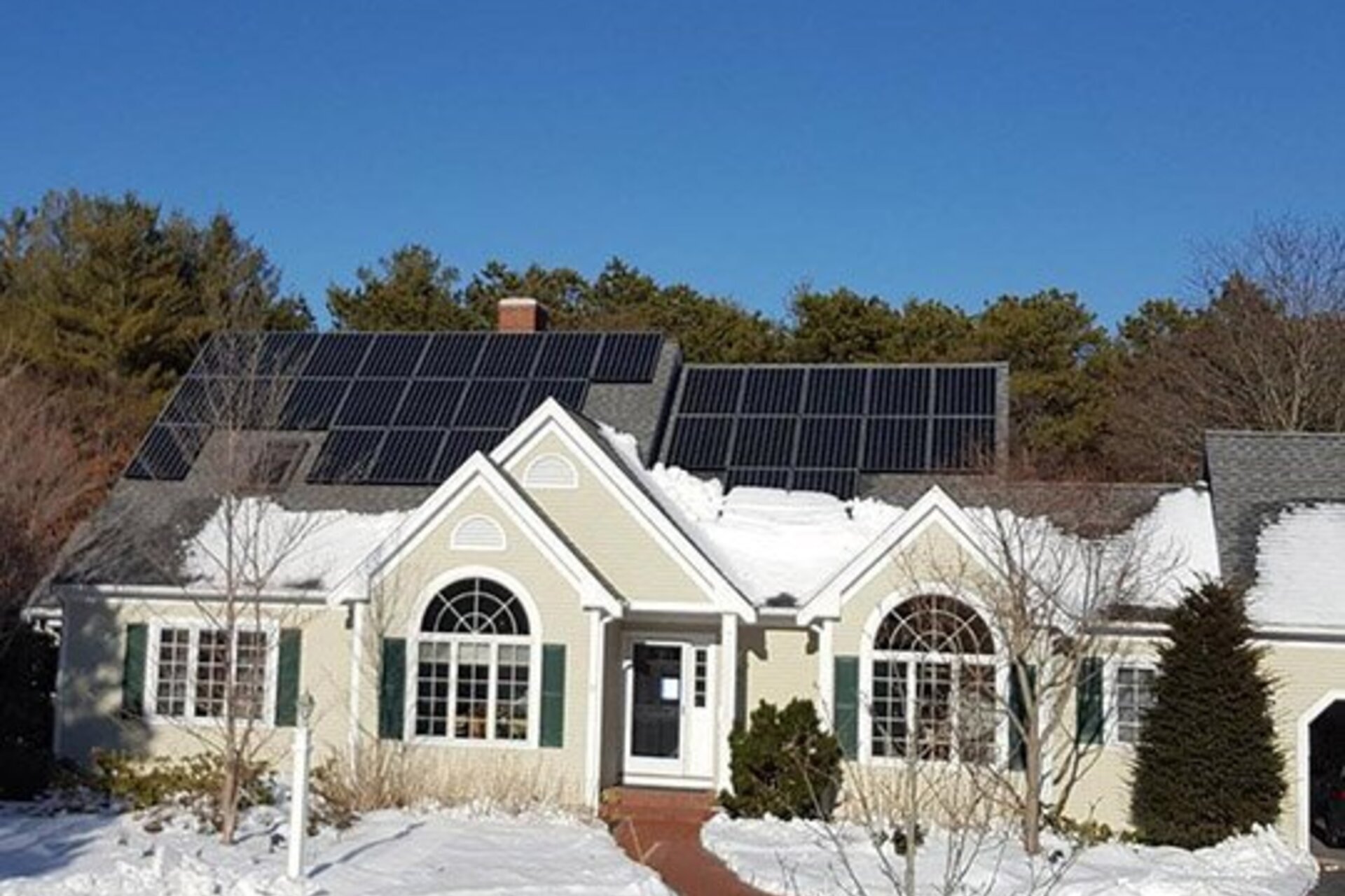 A house with solar panels on the roof, with snow on the lower half of the roof and covering the ground