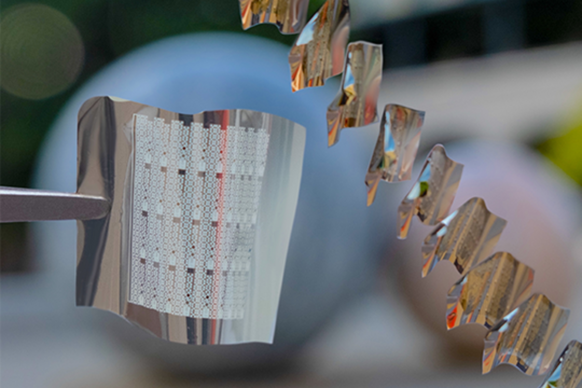 A flexible phase-change memory substrate held by tweezers (left) with a diagonal sequence showing substrates in the process of being bent.