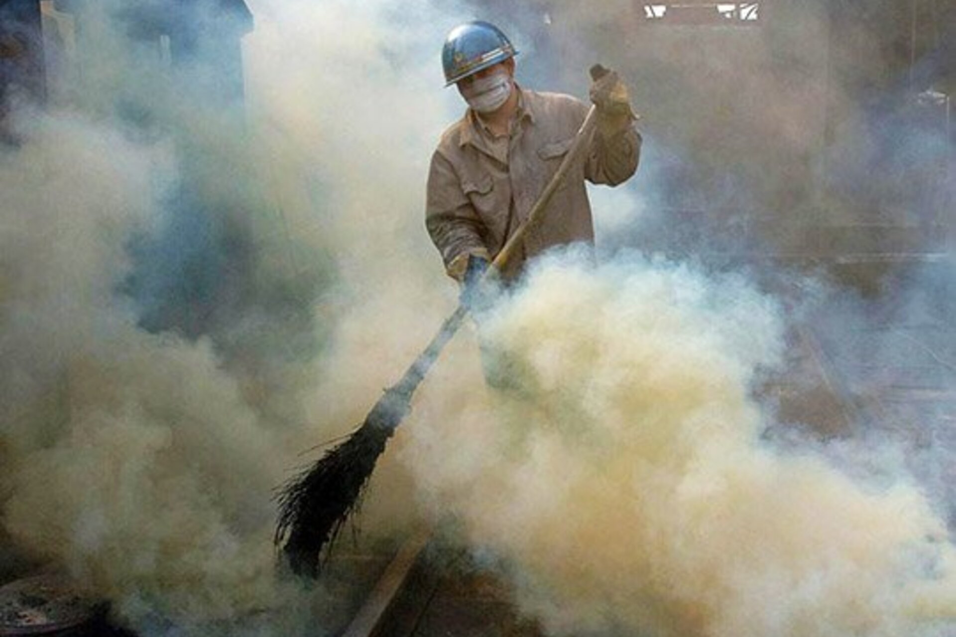 A man wearing a paper mask and a safety hat sweeps the floor by some rails in a steel mill in Hefei, China