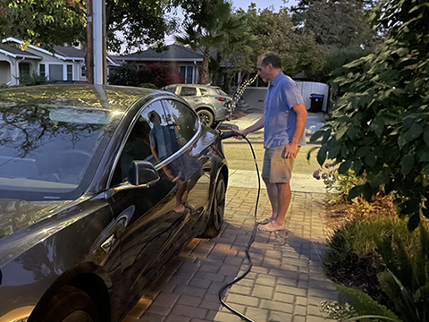 Man plugging charger into his EV in his driveway at sunset