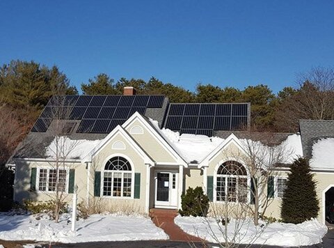 A house with solar panels on the roof, with snow on the lower half of the roof and covering the ground