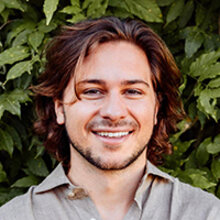 Alex Laplaza headshot standing before a wall of ivy