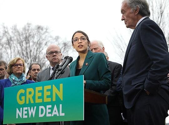 Alexandria Ocasio-Cortez speaks at a podium with a sign reading "Green New Deal"